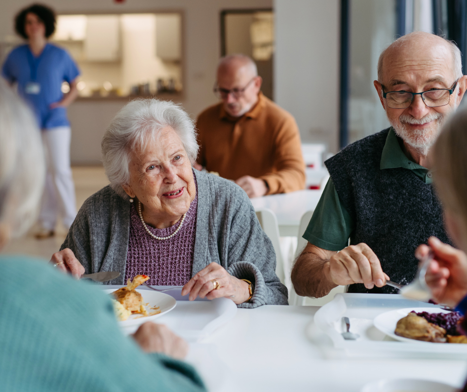 Smiling seniors enjoying a social meal together in a bright, modern West Palm Beach memory care community dining hall.