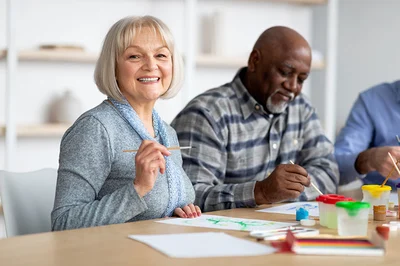 positive senior woman enjoying painting with brush